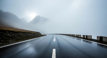 A wet, empty mountain road disappearing into the thick morning fog and clouds.