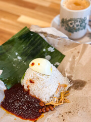 Classic Malaysian Nasi Lemak served on banana leaf and wax paper, featuring coconut rice, sambal, boiled egg, fried anchovies, and roasted peanuts.