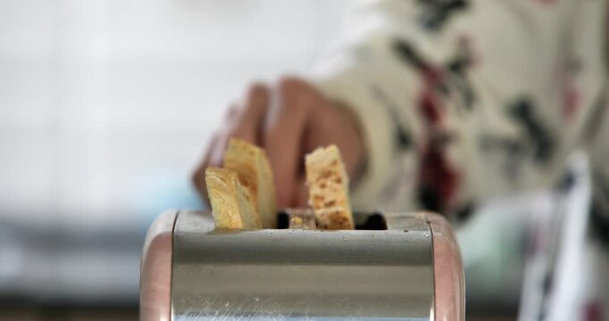 A close-up of a Caucasian woman putting two slices of bread into a toaster to make breakfast.