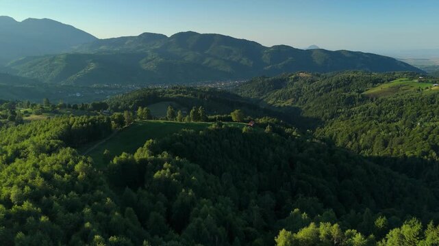 Late summer afternoon aerial over Simon hills, focusing on a hilltop meadow and animal shelter with Magurile Pietrei Craiului and Moieciu village in the background, Romania