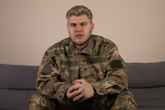 A man in a camouflage uniform aiming a rifle in a dense forest setting,