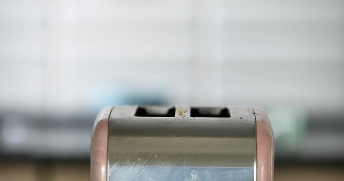 A photo of a toaster made of metal with a blurred background shows a woman walking through the kitchen.