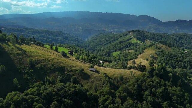 Carpathian hills above Simon with rustic animal shelters and freshly mown hayfields, Bran Rucar corridor and Piatra Craiului Mountains in warm summer light