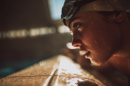 Close-up of focused swimmer at pool edge with water droplets on face and goggles, intense training moment captured in warm dramatic light