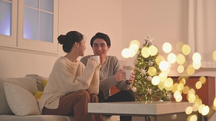 A cute couple spending Christmas in a room lit by the yellow glow of incandescent bulbs, watching TV and other media.