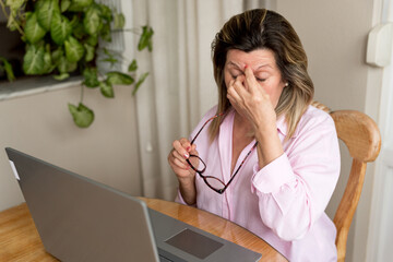 Woman feeling stressed and tired, rubbing eyes from headache during remote work on laptop at home