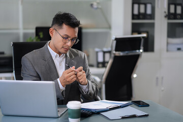 Asian businessman working at office with laptop and documents on table.