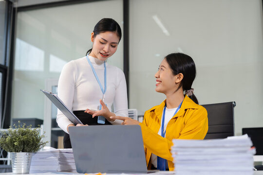 Asian manager mentor talking to young Asian female coworker, showing online project results at meeting. Two happy diverse professional executives team working in office using pc laptop.