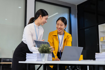 Asian manager mentor talking to young Asian female coworker, showing online project results at meeting. Two happy diverse professional executives team working in office using pc laptop.