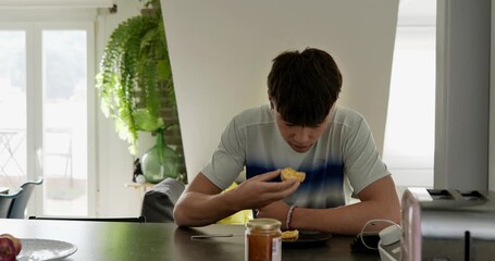 Teenager eating jam toast for breakfast. A young man enjoys a morning meal of bread and jam at the kitchen counter.