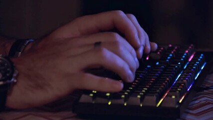 Closeup of a persons hands typing on a colorful illuminated keyboard in a dark room. - Powered by Adobe
