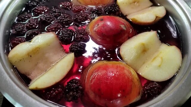 Apples and blackberries are boiled in water in a saucepan to make compote