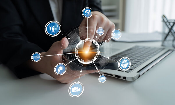 A business professional interacts with a smartphone while working on a laptop, surrounded by digital icons that symbolize technology, communication, and connectivity in an office environment. Crux
