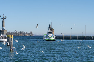 The catamaran ferry arrives in the wintery harbor, with seagulls circling overhead. Konstanz, Baden-Württemberg, Germany.