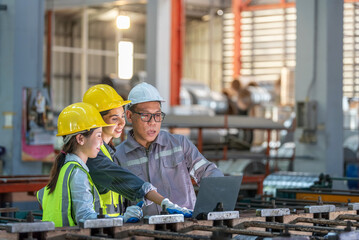 Engineers and workers wea safety helmets collaborating on industrial machinery in a factory setting with tools and equipment for manufactu and assembly