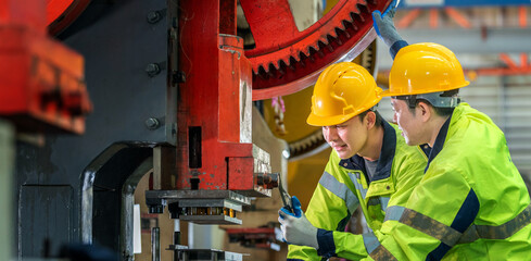 Two male industrial workers wea safety helmets and high visibility jackets inspecting and operating...