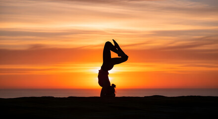 Silhouette of a woman performing a yoga headstand against a vibrant sunset sky over the ocean