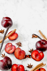 Fresh whole and halved red plums arranged on marble and dark surfaces, with optional spices and cutting board elements. Ideal for food styling, seasonal fruit themes and recipe content.