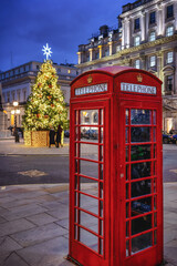 A christmas scene in London, England, with a classic, red telephone booth in front of a decorated Christmas tree during dusk