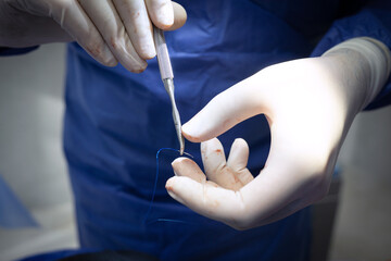 The doctor is holding a medical needle and surgical instruments, suturing a patient's wound in the operating room.