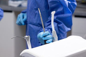 Medical theme, female hands wearing gloves and a surgical gown, holding a saliva ejector, dentistry.