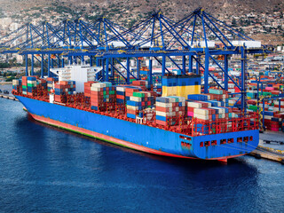 Aerial view of  a container super cargo ship being unloaded and loaded by cranes and trucks in a...