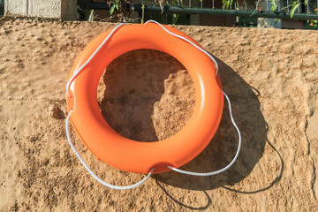 Orange life buoy hanging on sunlit concrete wall