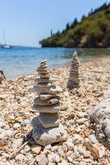 Balanced stone cairns on a pebble beach with clear blue sea and distant sailboat.