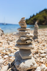 Balanced stone cairns on a pebble beach with clear blue sea and distant sailboat.