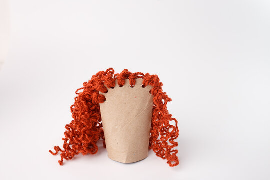Whimsical toilet paper roll craft with curly yarn hair, ideal for preschool education, DIY blogs, eco-friendly brands, creative workshops, and playful marketing visuals.