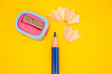 Blue pencil and a pink-blue sharpener with scattered shavings on a yellow background. Ideal for education, creativity and school stationery themes.