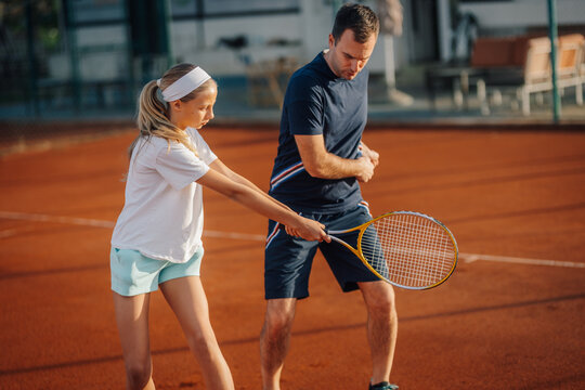Father teaching daughter tennis on clay court
