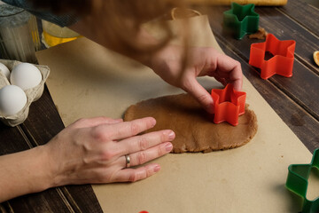 Making Christmas ginger cookies. Female hands using cookie cutters on rolled dough.