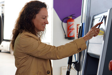 Smiling woman with curly hair paying with her cell phone at the gas station pump.