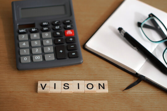 vision. financial concepts. wooden letters with calculator, notebook, and glasses in the background