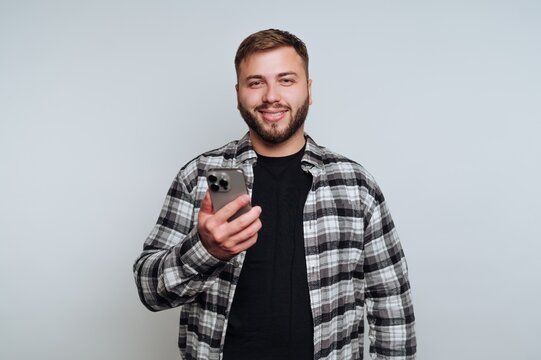 Smiling man holding phone and wearing checkered shirt in a simple background