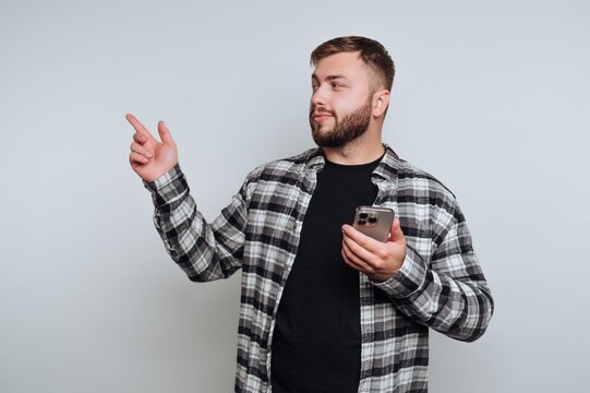 Man in checkered shirt gestures while holding smartphone against a light backdrop indoors