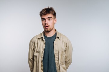 Surprised young man stands with hands behind his back against a plain backdrop in a studio setting