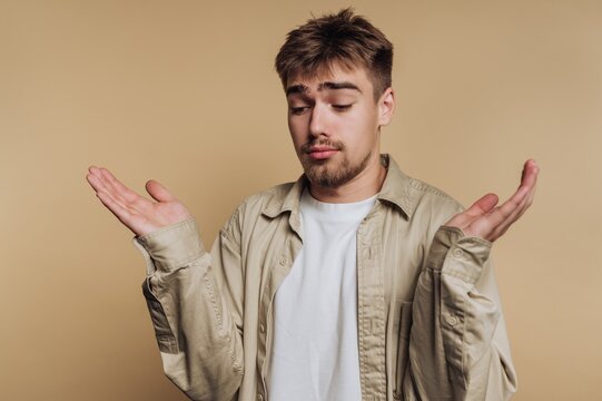 Young man expressing uncertainty with hands raised in a neutral setting