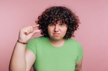 Person with curly hair making a gesture to indicate small size against a pink background