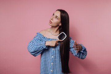 Young woman with long hair brushes her hair against a pink backdrop during a casual indoor setting