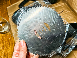 Close-up view of a hand holding a circular saw blade with protective packaging in a workshop setting