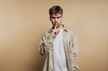 Young man holding his finger to his lips in a quiet gesture against a plain background