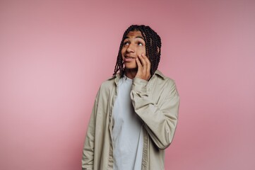 Young person with braided hair poses in front of a pink background displaying a thoughtful expression