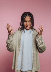 Portrait of young man expressing frustration with hands raised in front of pink backdrop
