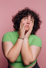 Young woman with curly hair expresses frustration against a pink background