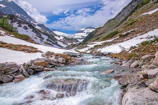 Alpine meltwater stream flowing through wide snowy valley