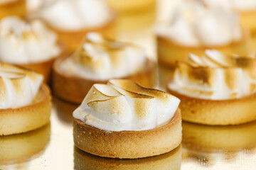 Close-up view of gourmet lemon meringue tartlets arranged on a golden tray during a catered reception, highlighting elegant dessert preparation.