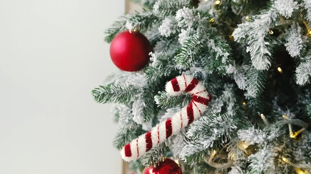Close up festive green pine tree branches decorated with fake snow, red balls and candy canes