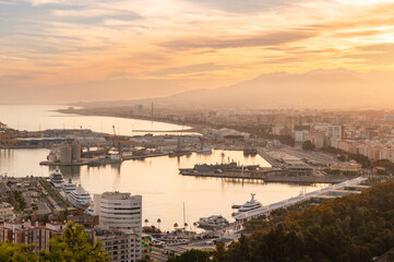 View of port with buildings, embankment, cranes, boats and yachts in Malaga city at golden hour, Andalusia, Spain. Cityscape at sunset.